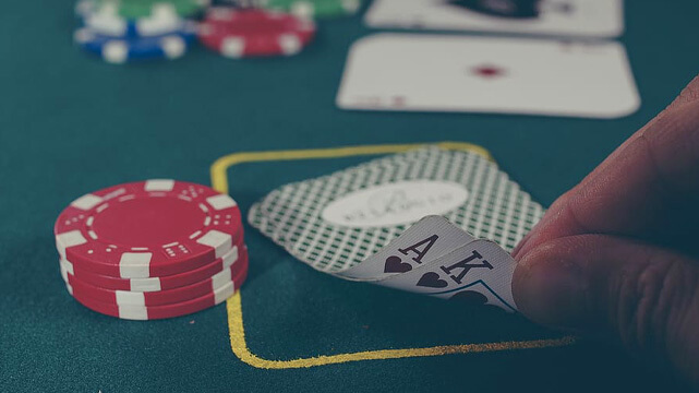 Hand Reaching for Two Poker Cards on Table