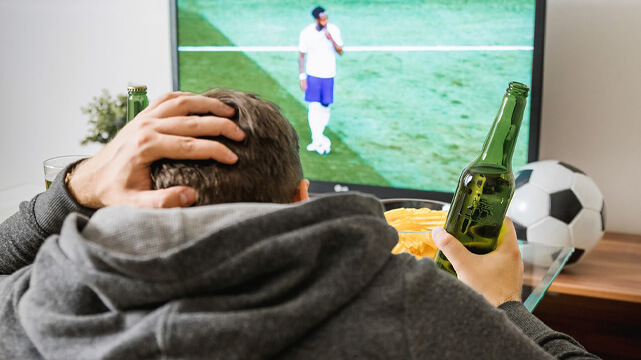 Guy Sitting on Couch Scratching Head, Watching Live Soccer Game