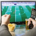 Person's Hands Holding Remote, Watching Football on TV